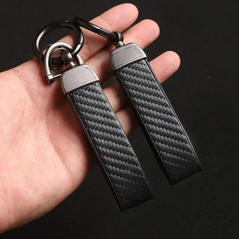 A close-up of a black carbon fiber leather keychain attached to a metal ring, held in a hand.