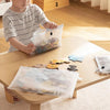 A child is using a clear mesh zipper pouch to store small items on a wooden table.