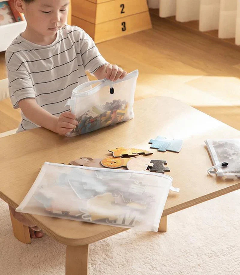 A child is using a clear mesh zipper pouch to store small items on a wooden table.