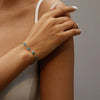 A close-up of a hand wearing a blue evil eye charm bracelet with an adjustable chain.