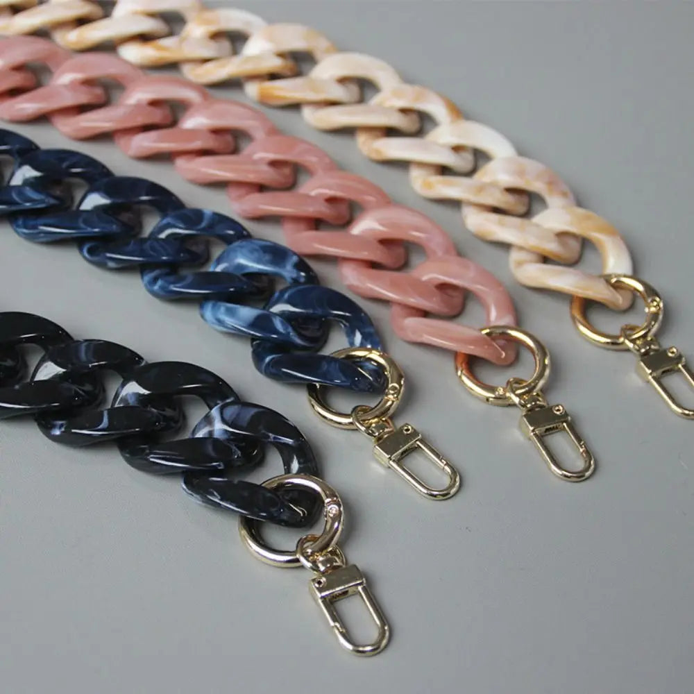 A close-up of several acrylic resin detachable bag chain straps in various shades of pink, beige, and blue on a gray backgrou