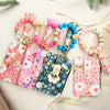 A set of silicone bead and PU leather key chain wallets in pink, floral, and blue colors with decorative tassels.