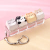A row of pink and cream cat-themed keycaps or fidget toys displayed on a clear plastic tray with a silver bag charm.