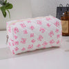Bolsa acolchada blanca para maquillaje con estampado de lazo rosa y cremallera sobre una superficie blanca.