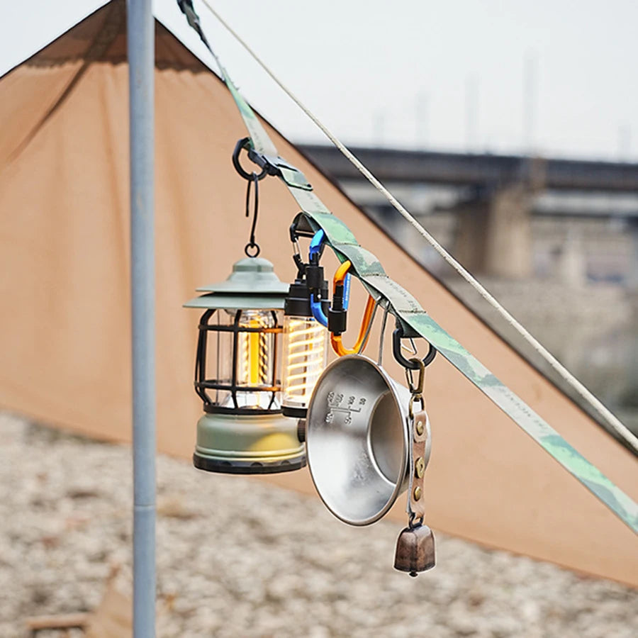 A durable outdoor camping crossbody strap with a lantern and a metal bell hanging from it.