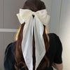 A woman with long brown hair tied in a ponytail wearing an elegant white silk bow hair clip.