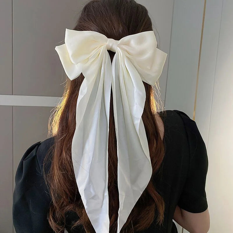 A woman with long brown hair tied in a ponytail wearing an elegant white silk bow hair clip.
