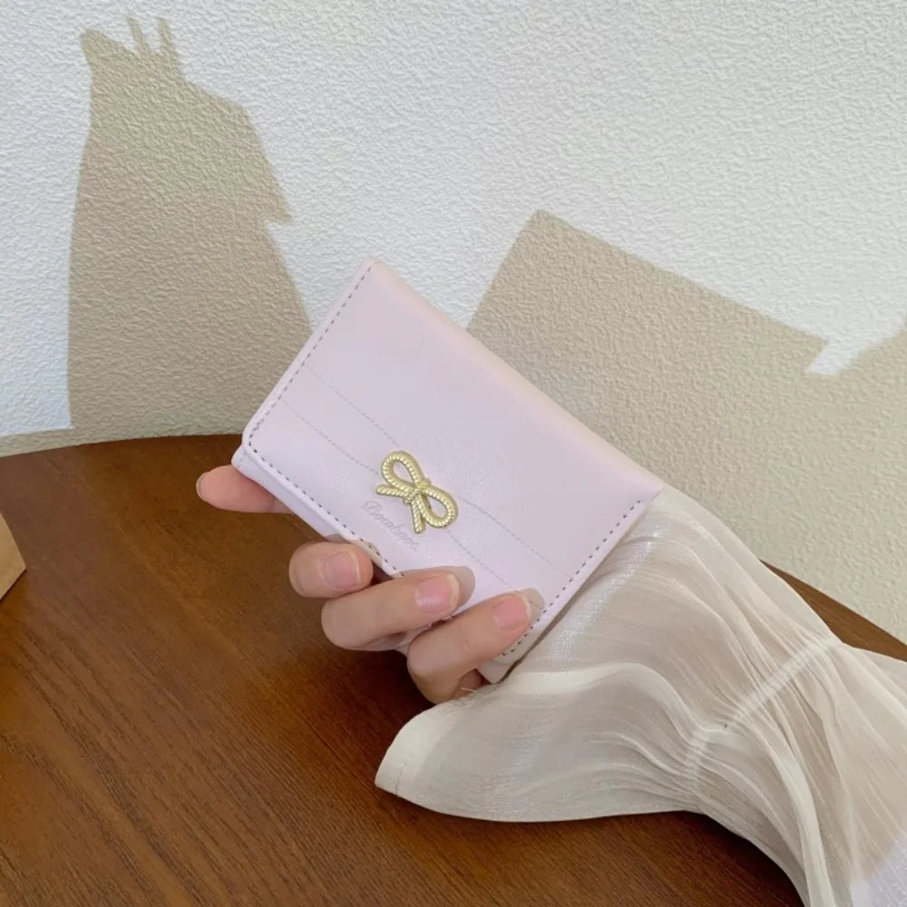 Une main tient un porte-cartes tri-pli en PU rose pâle sur une surface en bois.