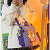 A person holds a purple Dora The Explorer cartoon flannel backpack against an orange background.