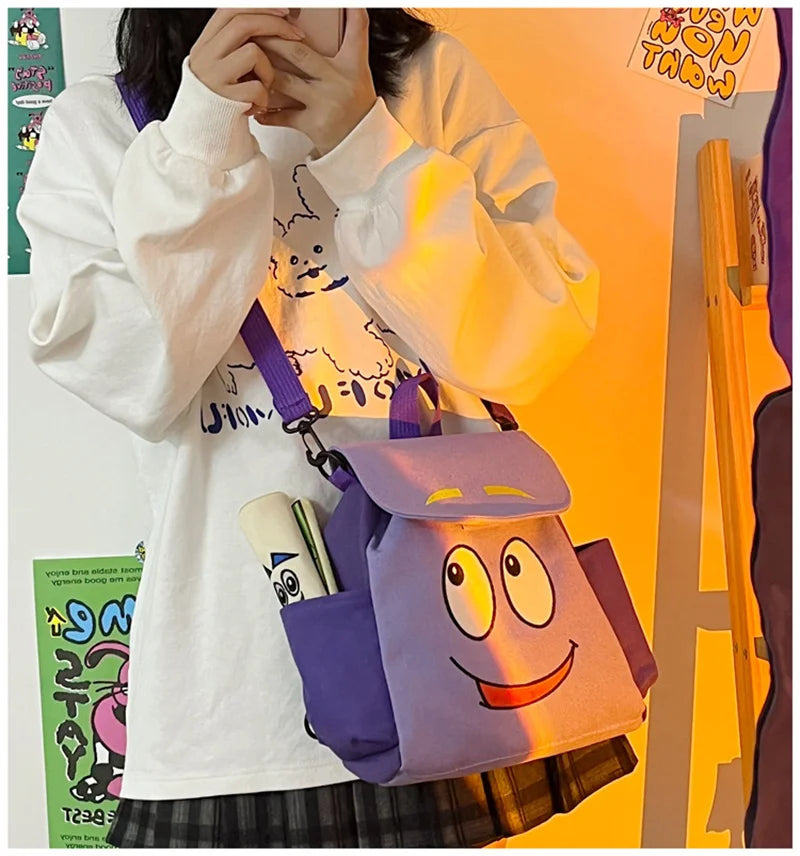 A person holds a purple Dora The Explorer cartoon flannel backpack against an orange background.