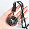 A black alloy wheel hub brake disc rearview mirror pendant with a coiled spring chain on a hand.