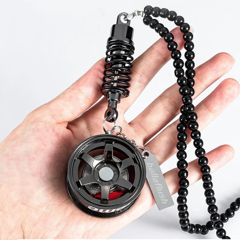 A black alloy wheel hub brake disc rearview mirror pendant with a coiled spring chain on a hand.