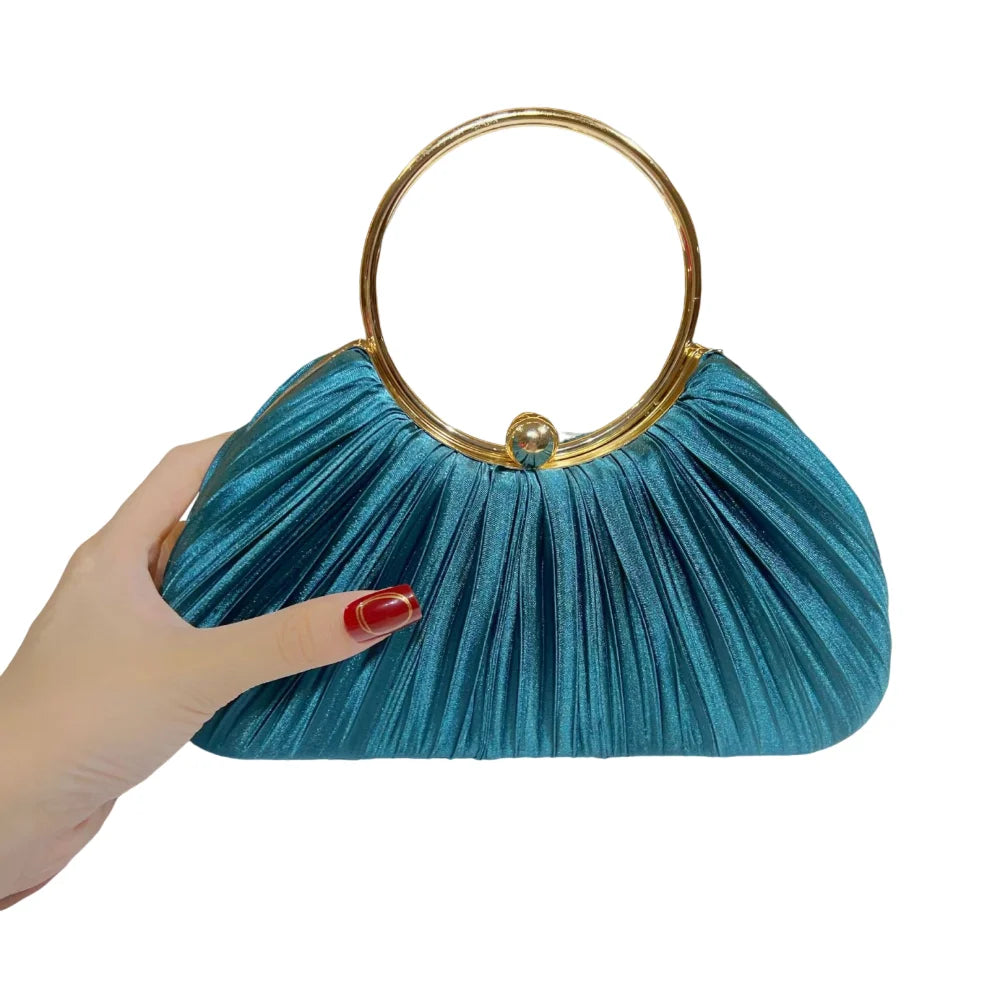 A teal satin pleated evening clutch bag with a gold rim is held by a hand.