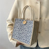 A beige blazer sleeve holds a patterned floral linen tote bag with natural twine handles.