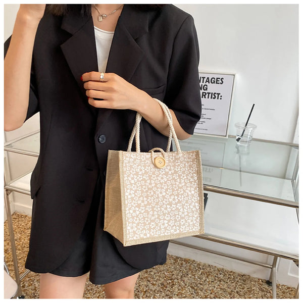 A woman holds a beige floral linen tote bag with secure closures against a white background.