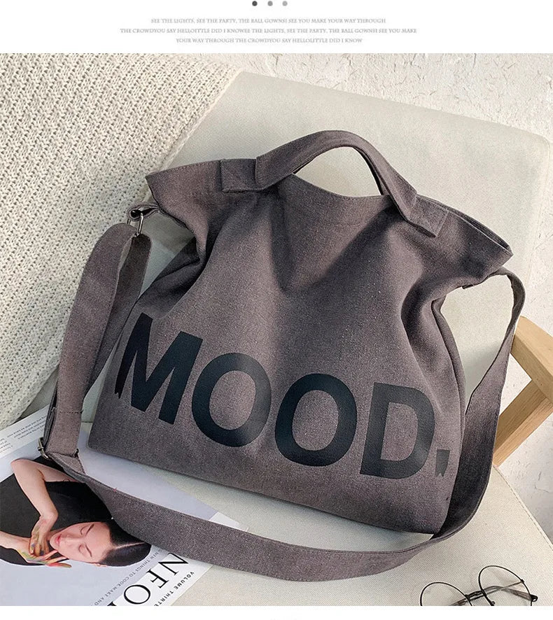 A dark gray canvas tote bag featuring the word MOOD printed in large black letters, resting on a light surface.