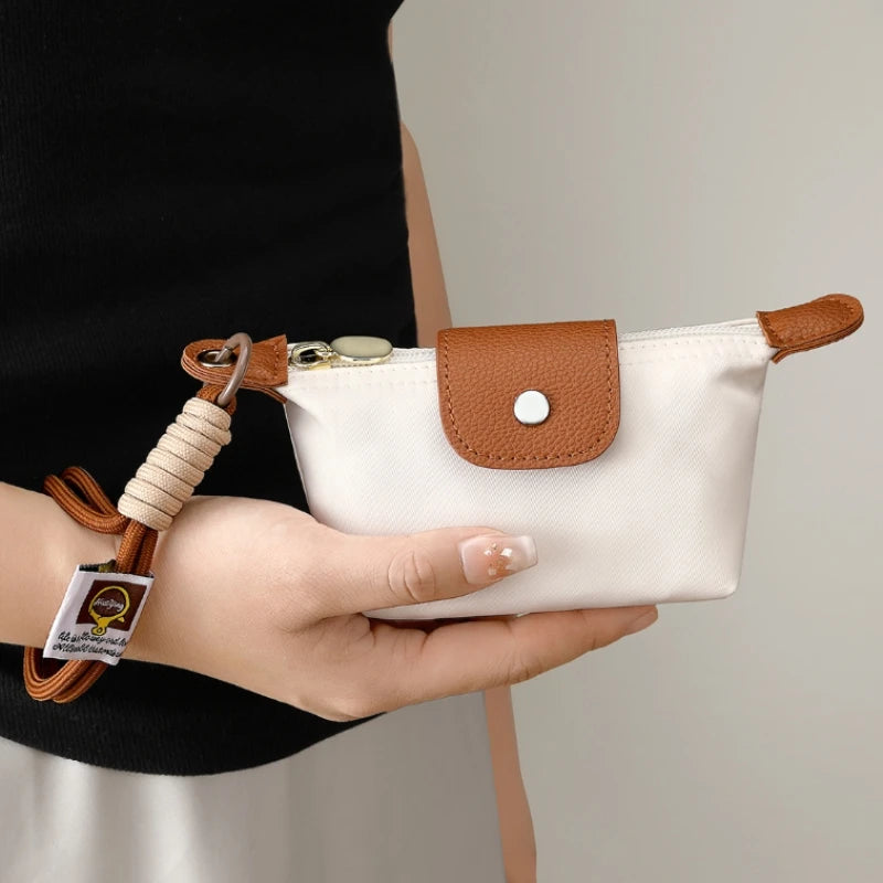 Eine Hand hält eine beige Leder-Geldbörse mit brauem Verschluss und Armband vor einem hellen Hintergrund.