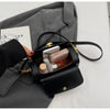 A black textured leather shoulder bag with gold hardware resting on a gray suit jacket.