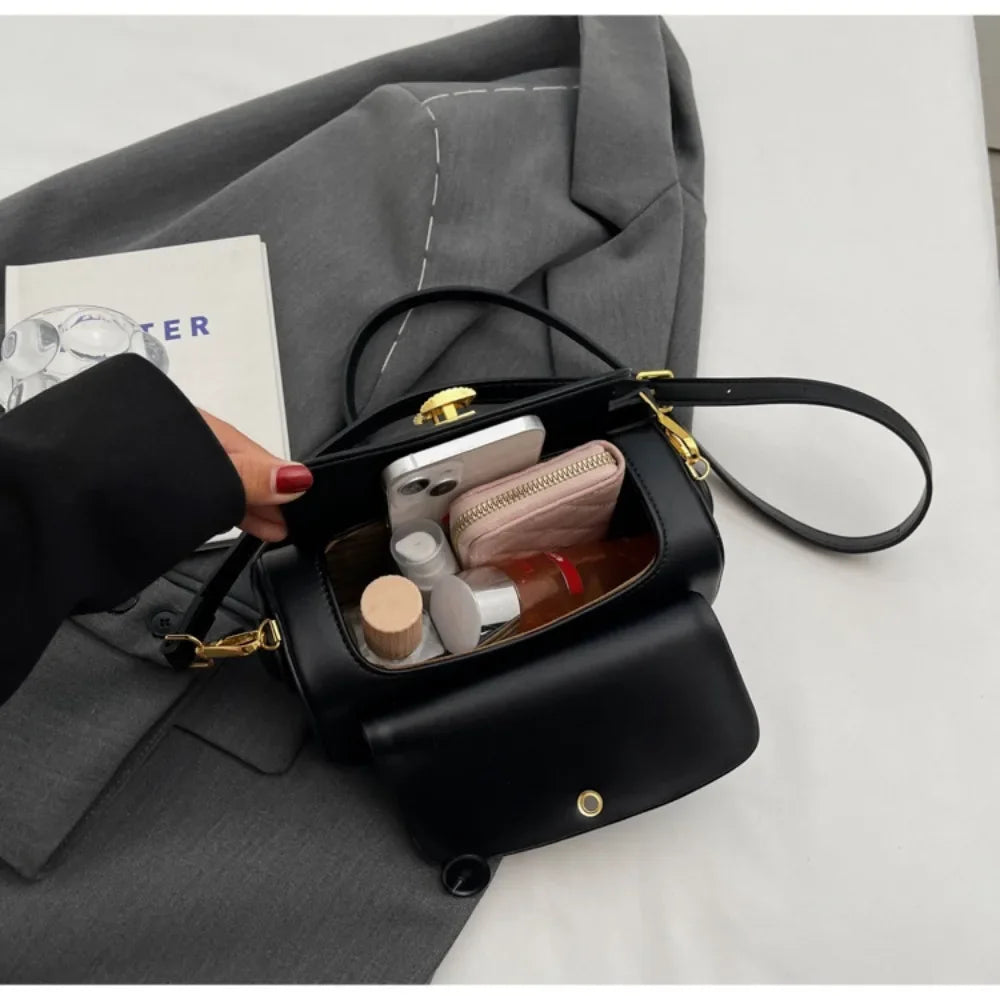 A black textured leather shoulder bag with gold hardware resting on a gray suit jacket.
