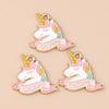 Two gold-toned unicorn horse charm pendants with pink and iridescent accents on a beige background.