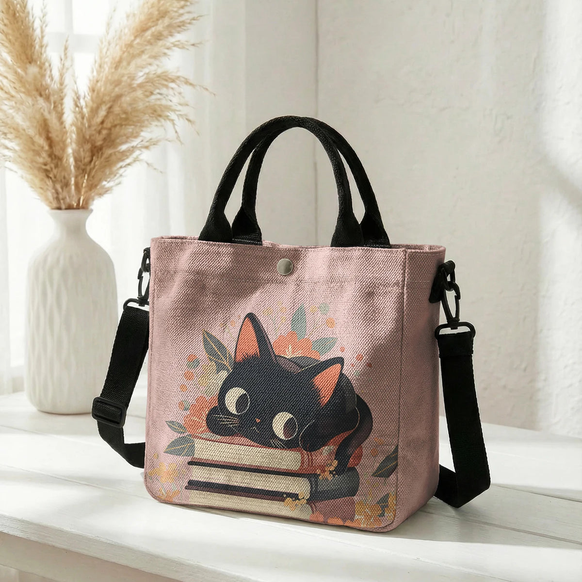 Pinke Tasche mit schwarzer Katzen- und Blumenmuster, schwarze Riemen, auf weißer Oberfläche.
