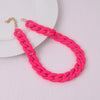 A bright pink acrylic statement choker necklace with a gold-colored chain is displayed on a white plate.