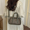 A woman holds a gray crocodile textured mini crossbody bag in a light beige trench coat.