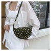 A woman wearing a white shirt and skirt holds a dark green faux suede crossbody bag with gold rivet accents.