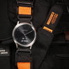 A black Garmin watch with an orange strap is shown on a black nylon sport strap.