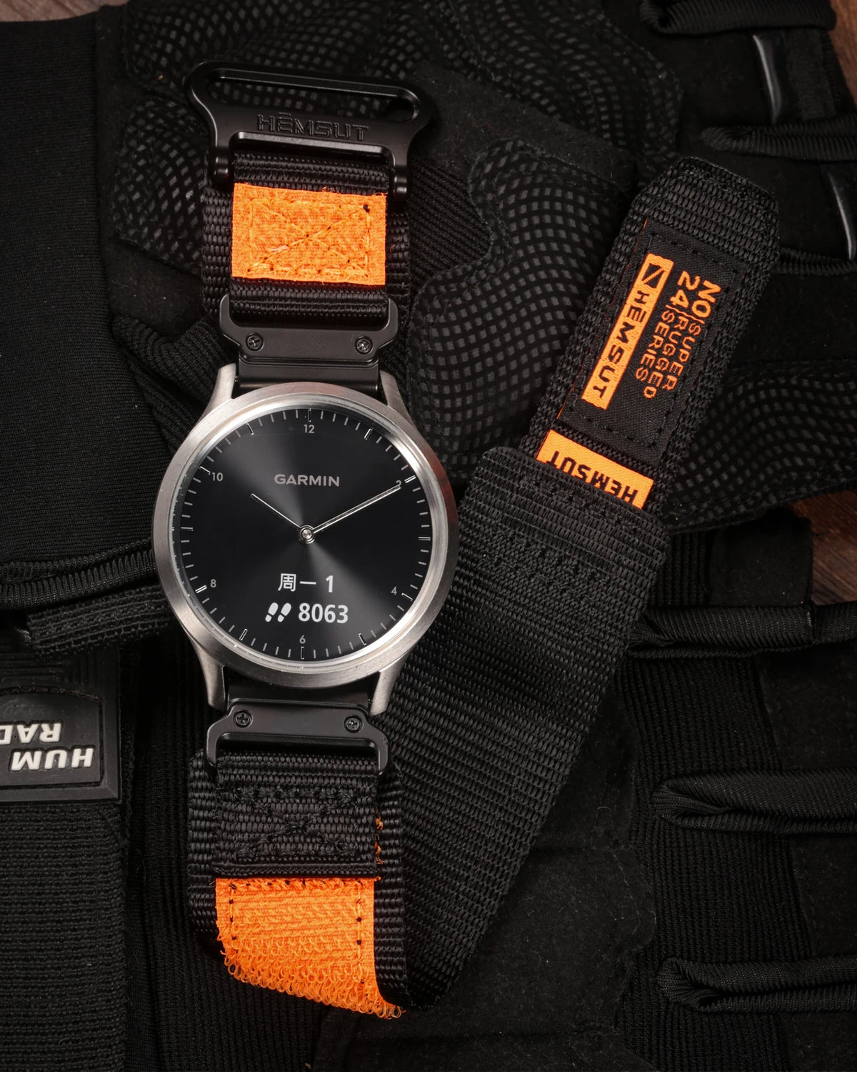 A black Garmin watch with an orange strap is shown on a black nylon sport strap.