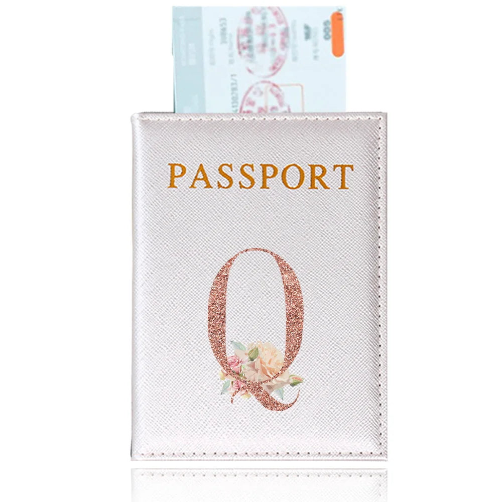 A pink leather passport holder with a gold embossed letter Q and floral design.