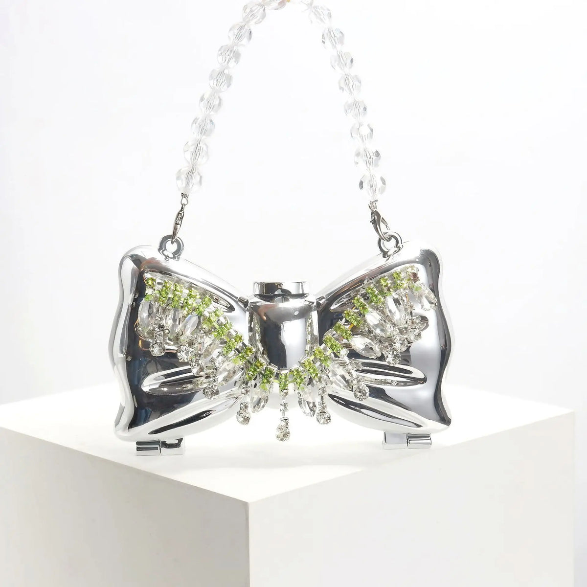 Silver acrylic bow clasp mini handbag with a clear crystal chain strap displayed on a white pedestal.