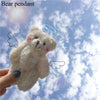 A fluffy white bear pendant is held against a blue sky with clouds.