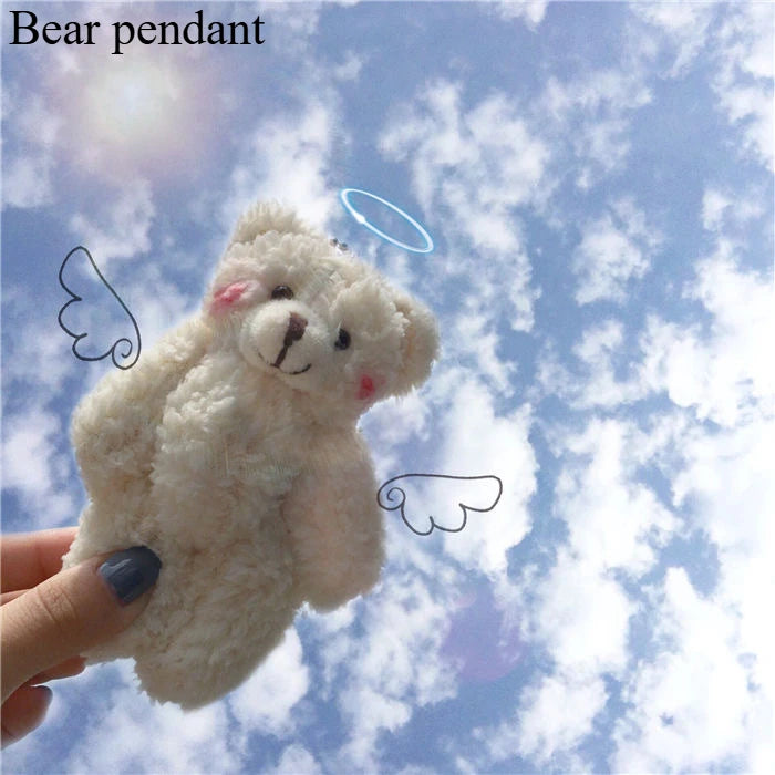 A fluffy white bear pendant is held against a blue sky with clouds.