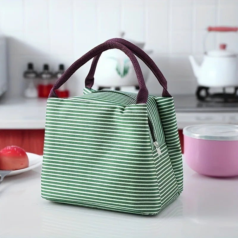 A green and white striped thermal lunch bag with dark purple handles resting on a white surface.