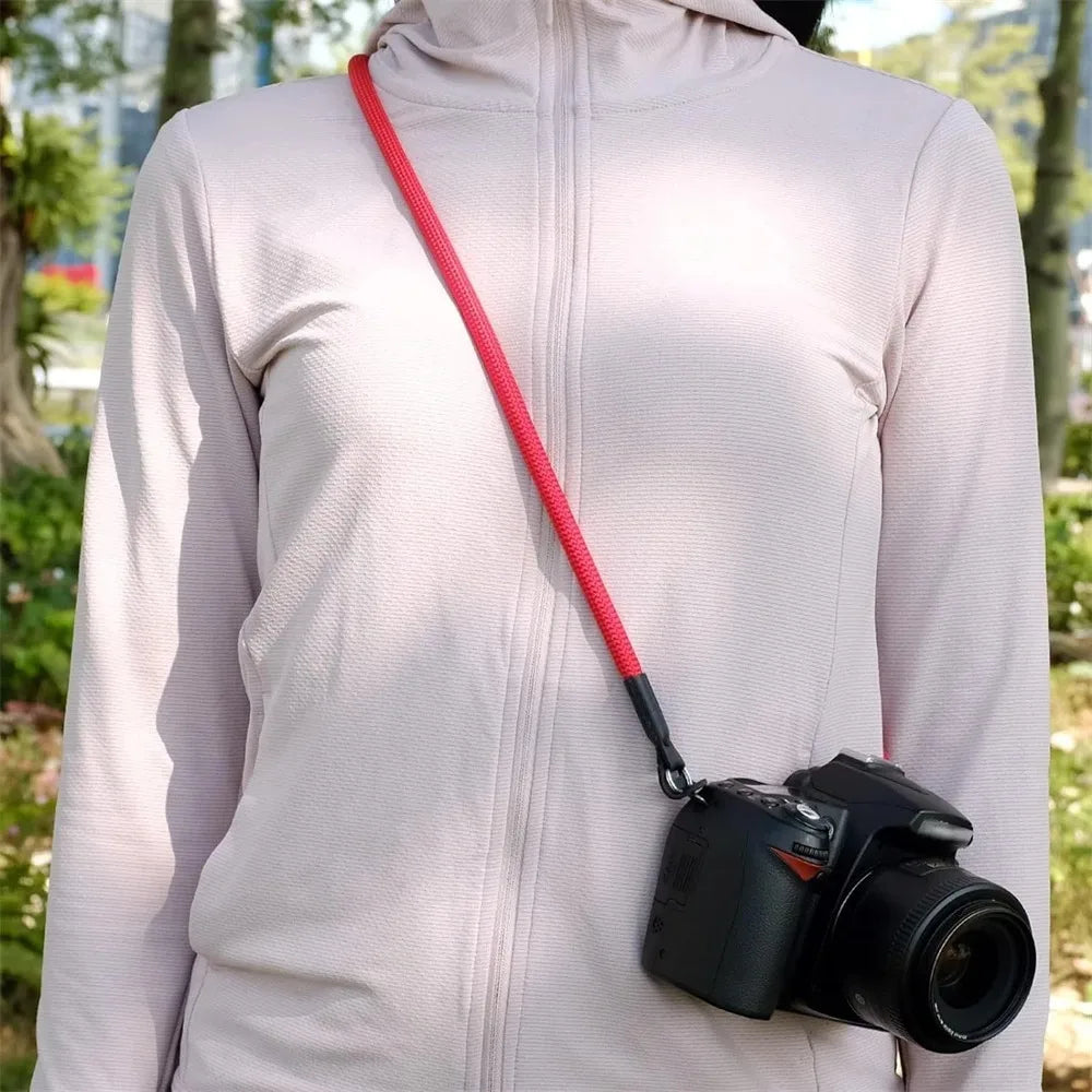 A person wearing a light pink jacket is holding an adjustable camera and DSLR shoulder strap.