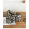 A leopard print riveted Boston shoulder bag resting on a wooden surface next to a book.