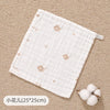 A white muslin baby burp cloth towel with small floral embroidery is shown on a beige textured surface.