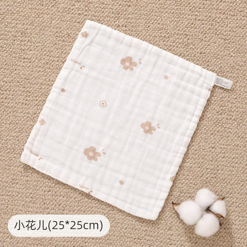 A white muslin baby burp cloth towel with small floral embroidery is shown on a beige textured surface.