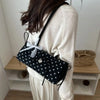 Schwarze Retro-Polka-Dot-Schultertasche mit weißer Spitzenverzierung, getragen von einer Person in einem hellen Pullover.