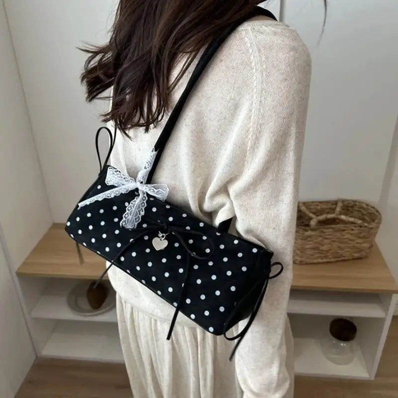 Schwarze Retro-Polka-Dot-Schultertasche mit weißer Spitze, getragen von einer Person in einem hellen Pullover.