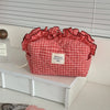 A red and white checkered makeup pouch with a ruffled lace trim resting on a white surface.