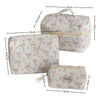 A set of three quilted cosmetic bags in white fabric with pink floral embroidery and light beige trim.