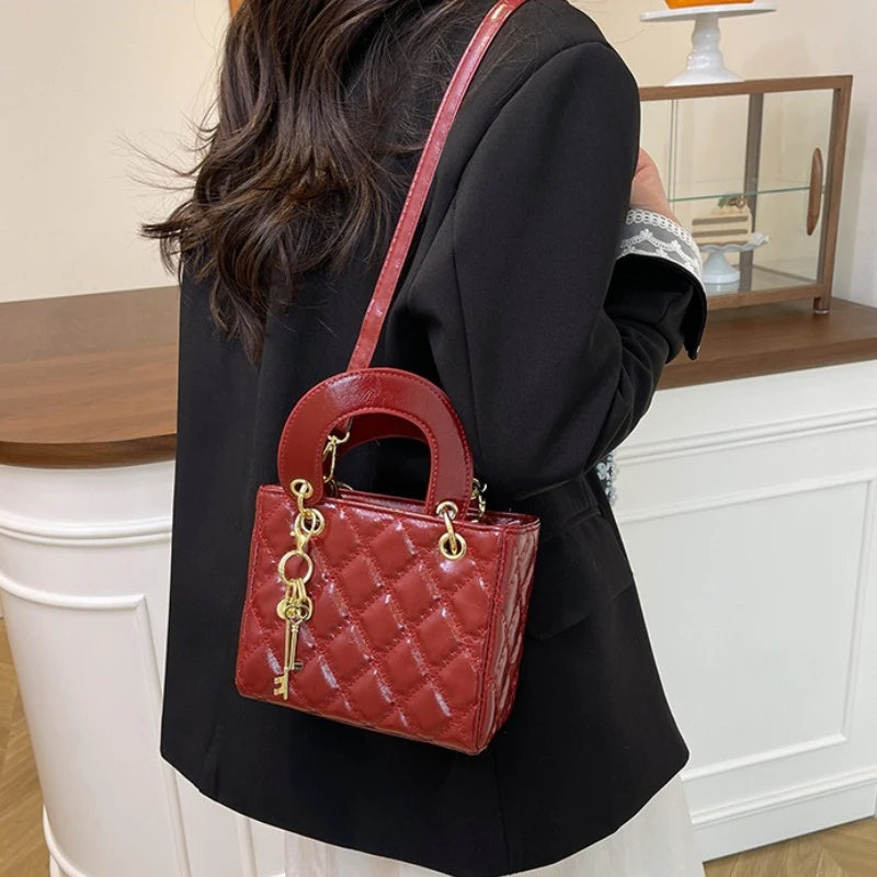A woman holds a red quilted leather crossbody handbag with gold chain accents against a white fireplace mantel.