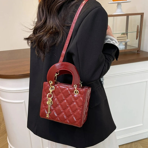 A woman holds a red quilted leather crossbody handbag with gold chain accents against a white fireplace mantel.