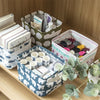 A collection of folded fabric items and storage baskets in various shades of green, white, and blue on a wooden surface.