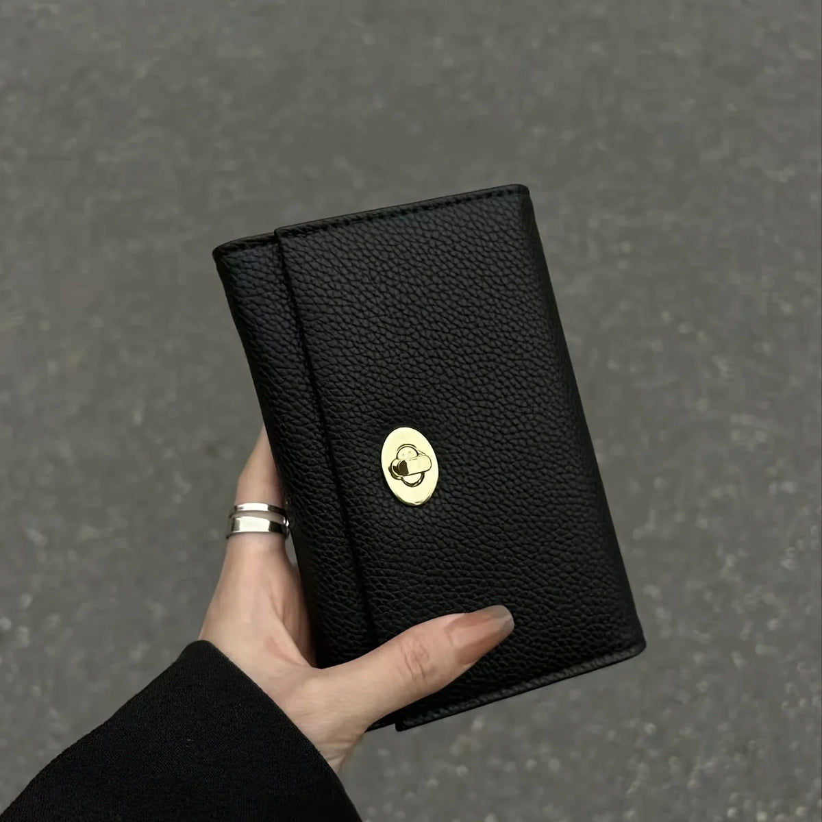 A hand holds a black compact women's card holder wallet with a gold cloud emblem.