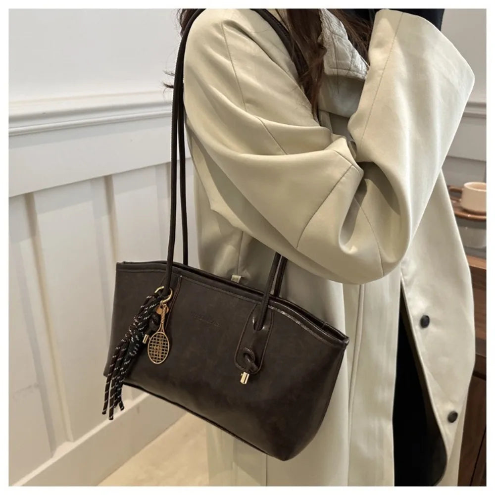 A woman holds a large black PU leather tote bag in front of a light beige trench coat.