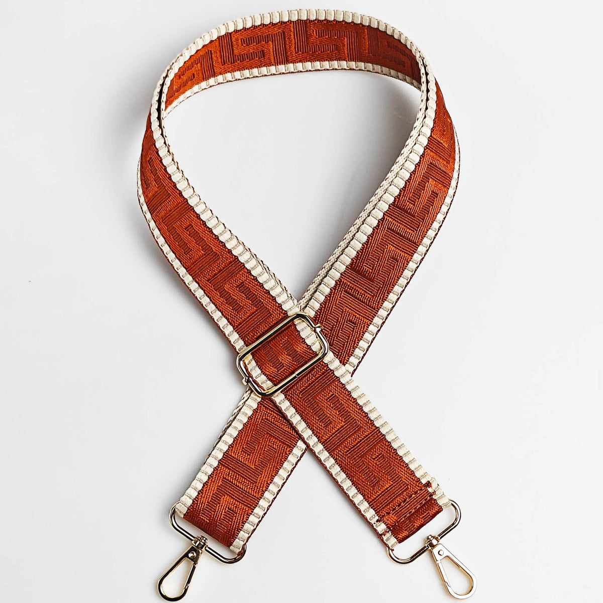 A brown and cream patterned adjustable crossbody bag strap with a gold buckle.