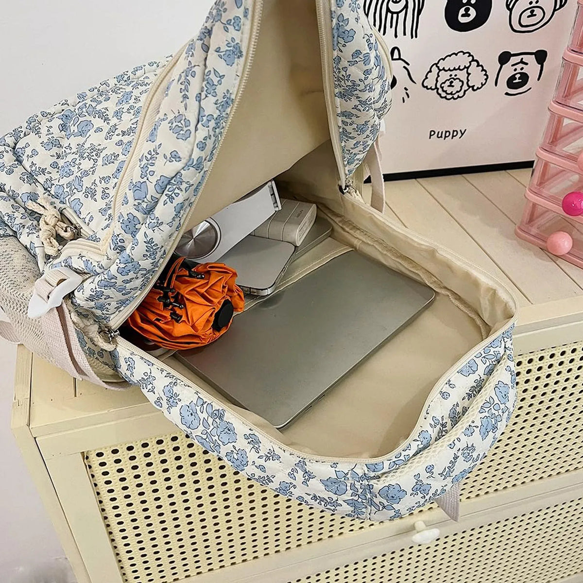 A light beige floral quilted backpack set with a laptop and accessories inside.
